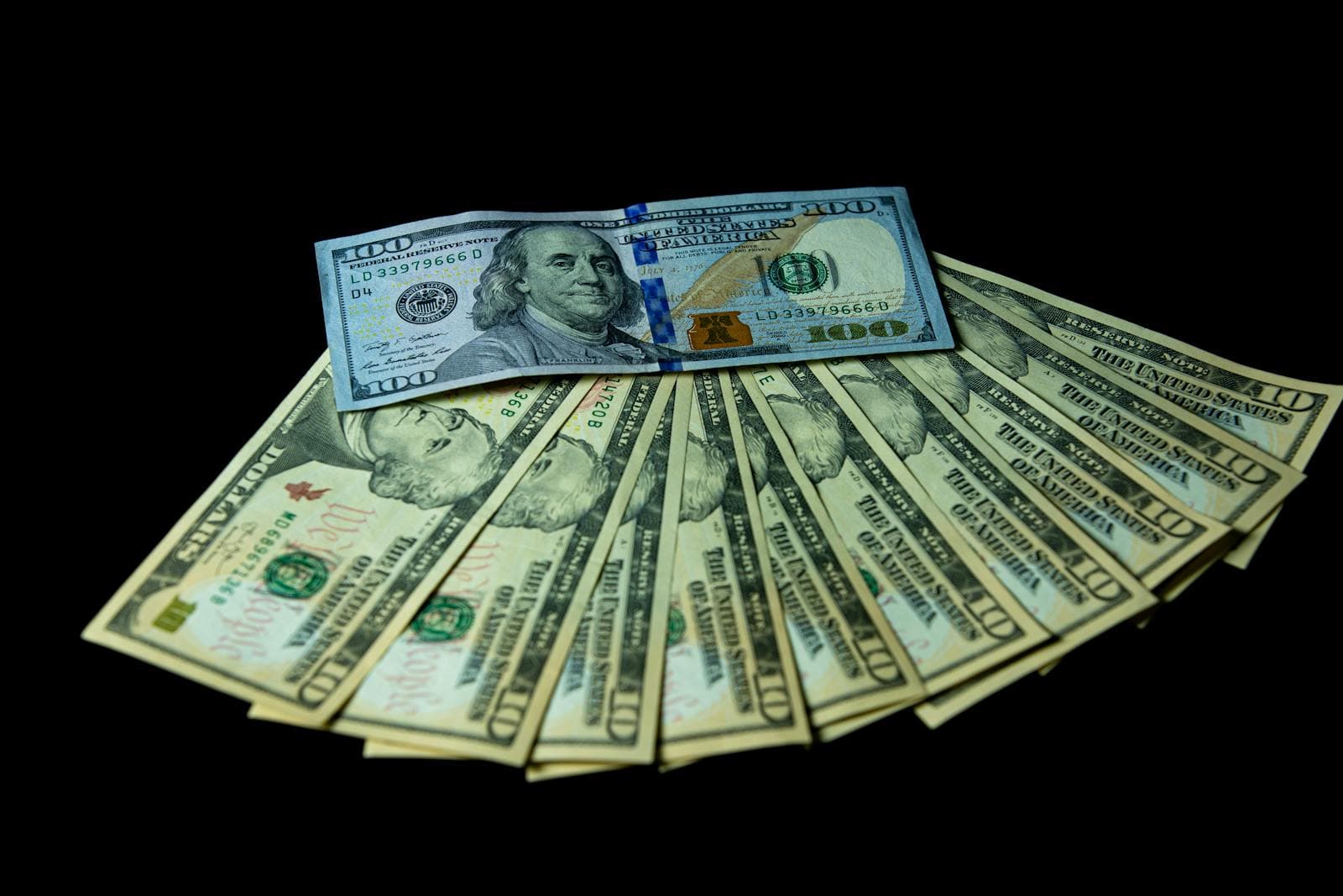 A fanned-out stack of U.S. hundred-dollar bills on a dark background.