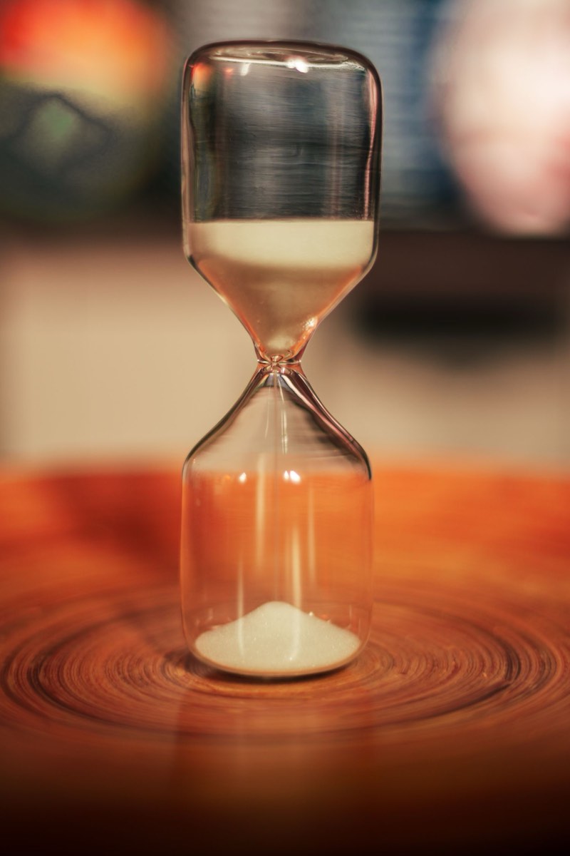 An hourglass on a wooden surface with most of its sand already run through.