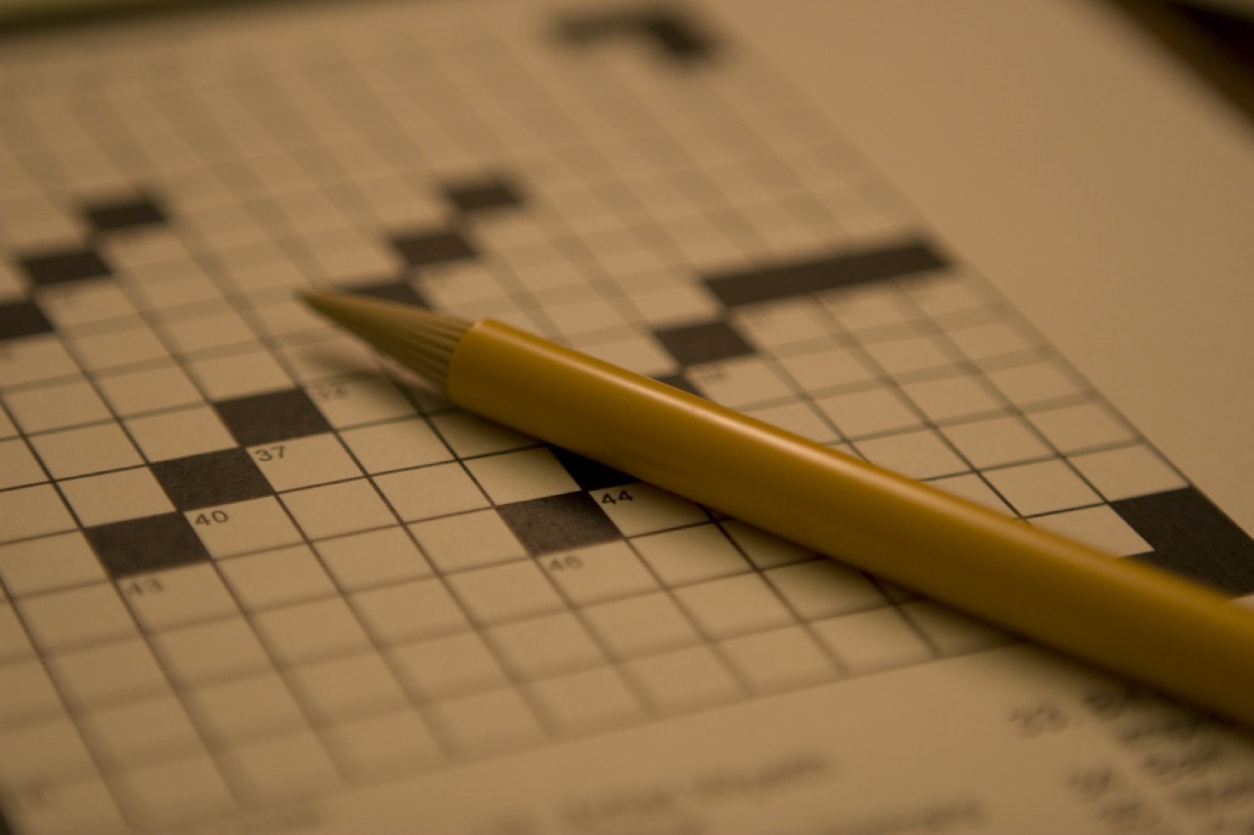 A yellow pencil resting on a blank crossword puzzle grid.