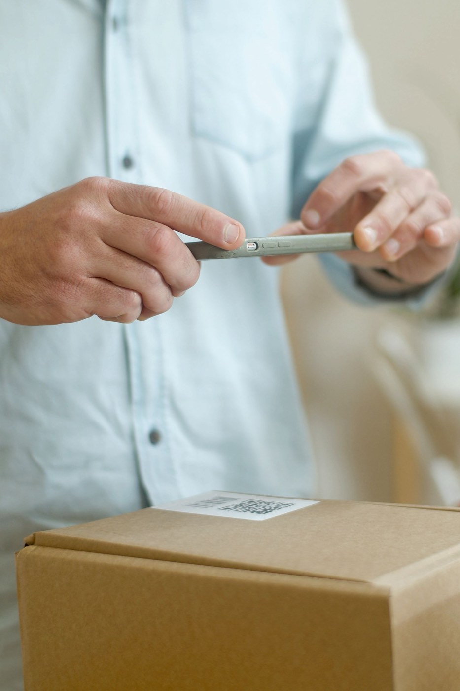 A person holding a phone over a barcode and QR label on a cardboard box.