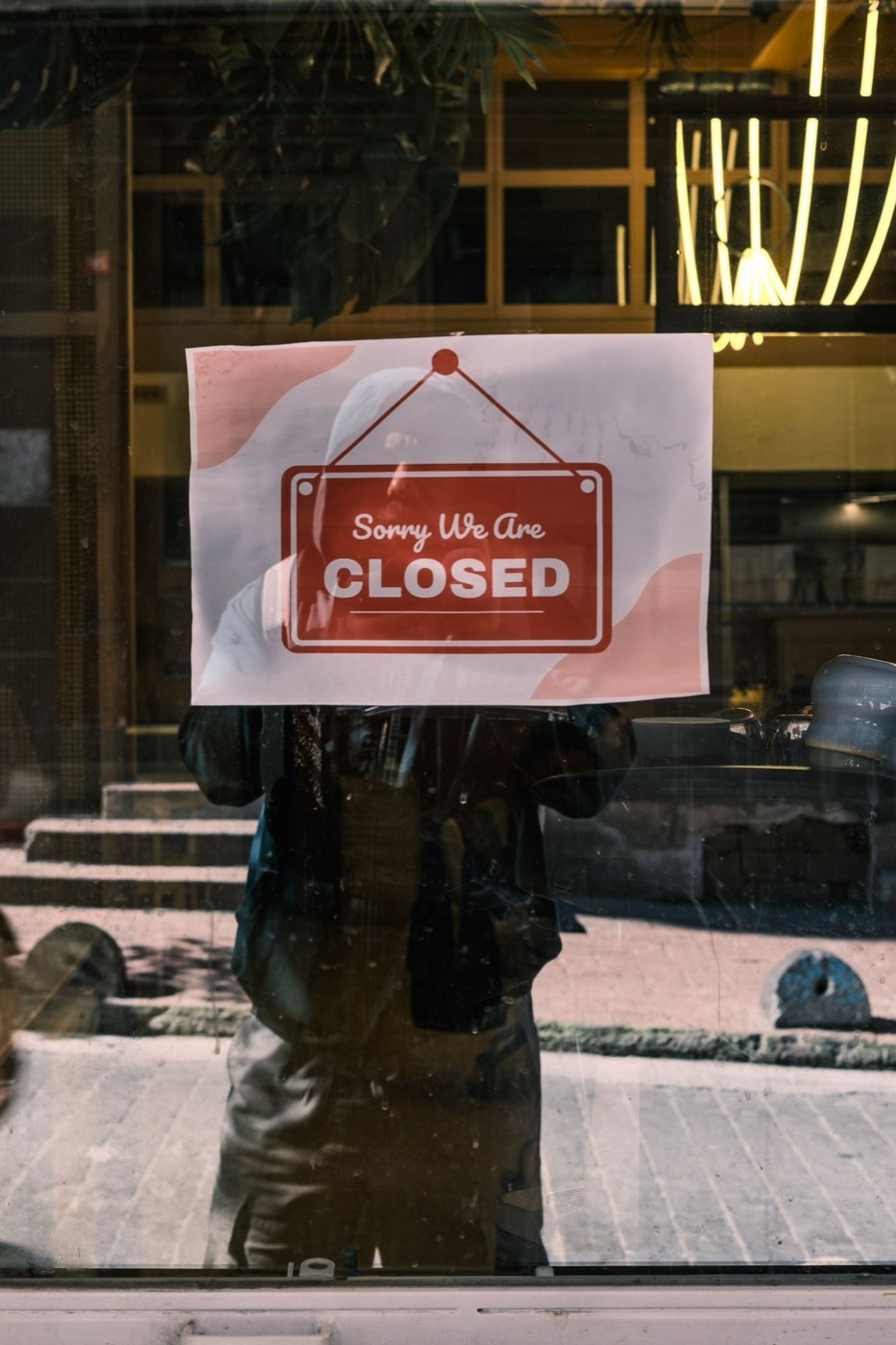 A Sorry We Are Closed sign taped inside a storefront window.