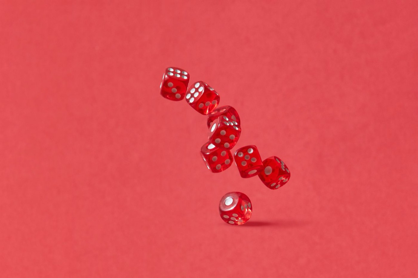 Red dice tumbling through the air against a flat red background.