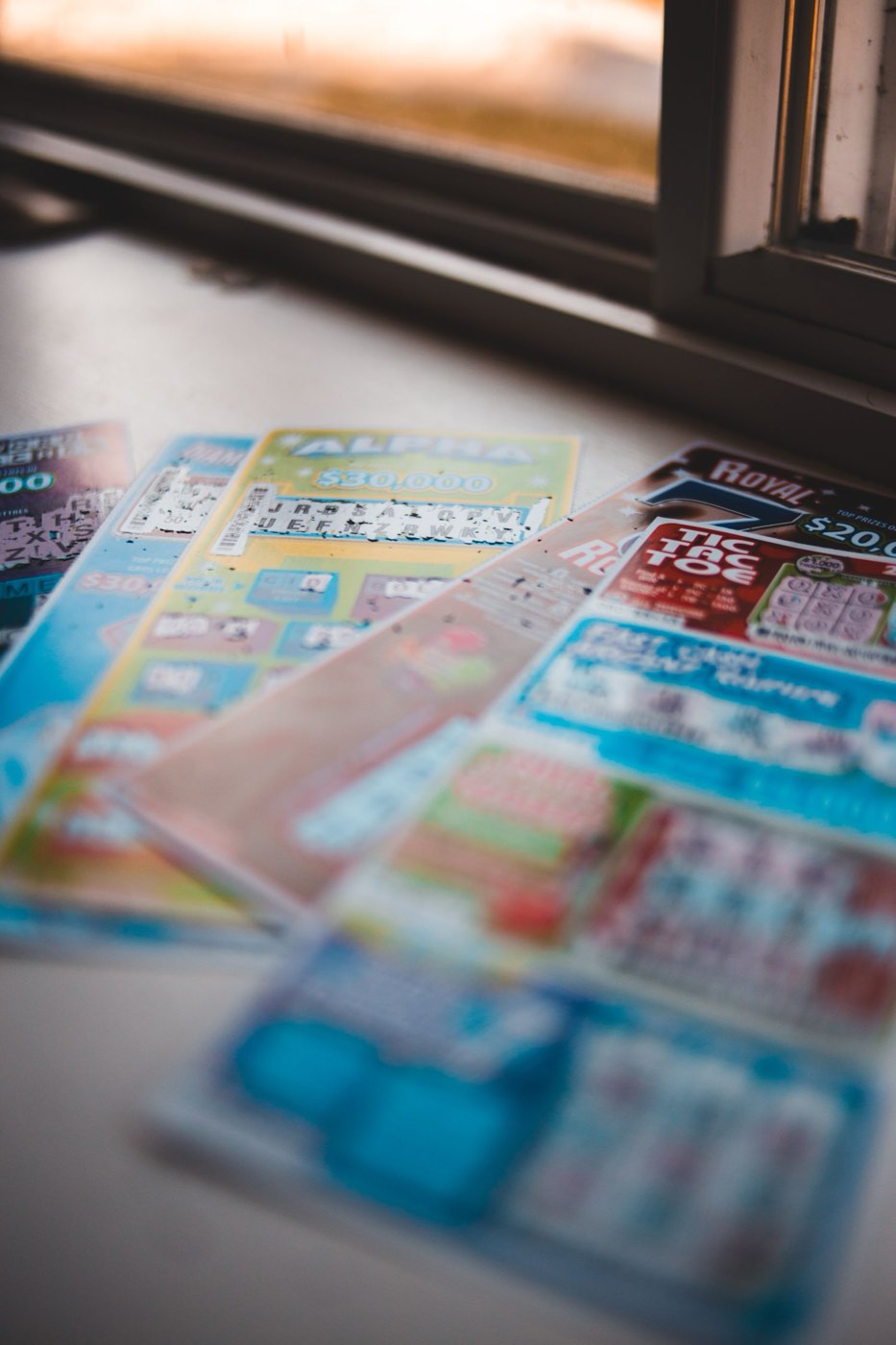 Several scratched lottery tickets fanned out on a white window sill in evening light.