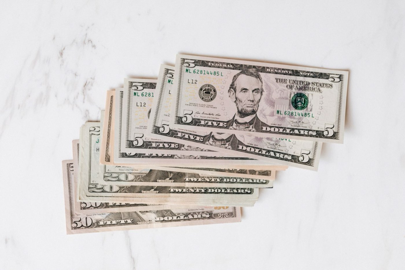 US banknotes in several denominations fanned out on a white marble surface.